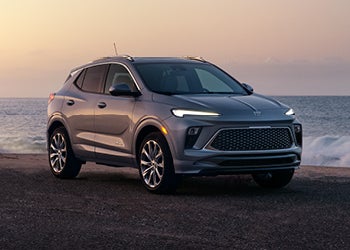 A sleek silver compact SUV parked on a coastal road at sunset, featuring modern LED headlights, a large patterned front grille, and sporty alloy wheels, with the ocean in the background.
