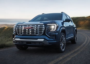 Dark blue GMC SUV driving on a coastal road at sunset