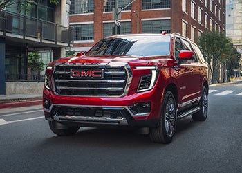 Red GMC SUV driving through a city street with buildings in the background
