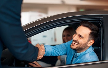 A man and woman shake hands inside a car, symbolizing a professional or friendly agreement.