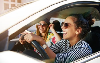 Two women in sunglasses are seated in a car, enjoying a drive together.