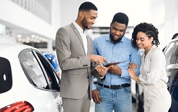Three individuals examining a car at a dealership, discussing features and options available for purchase.
